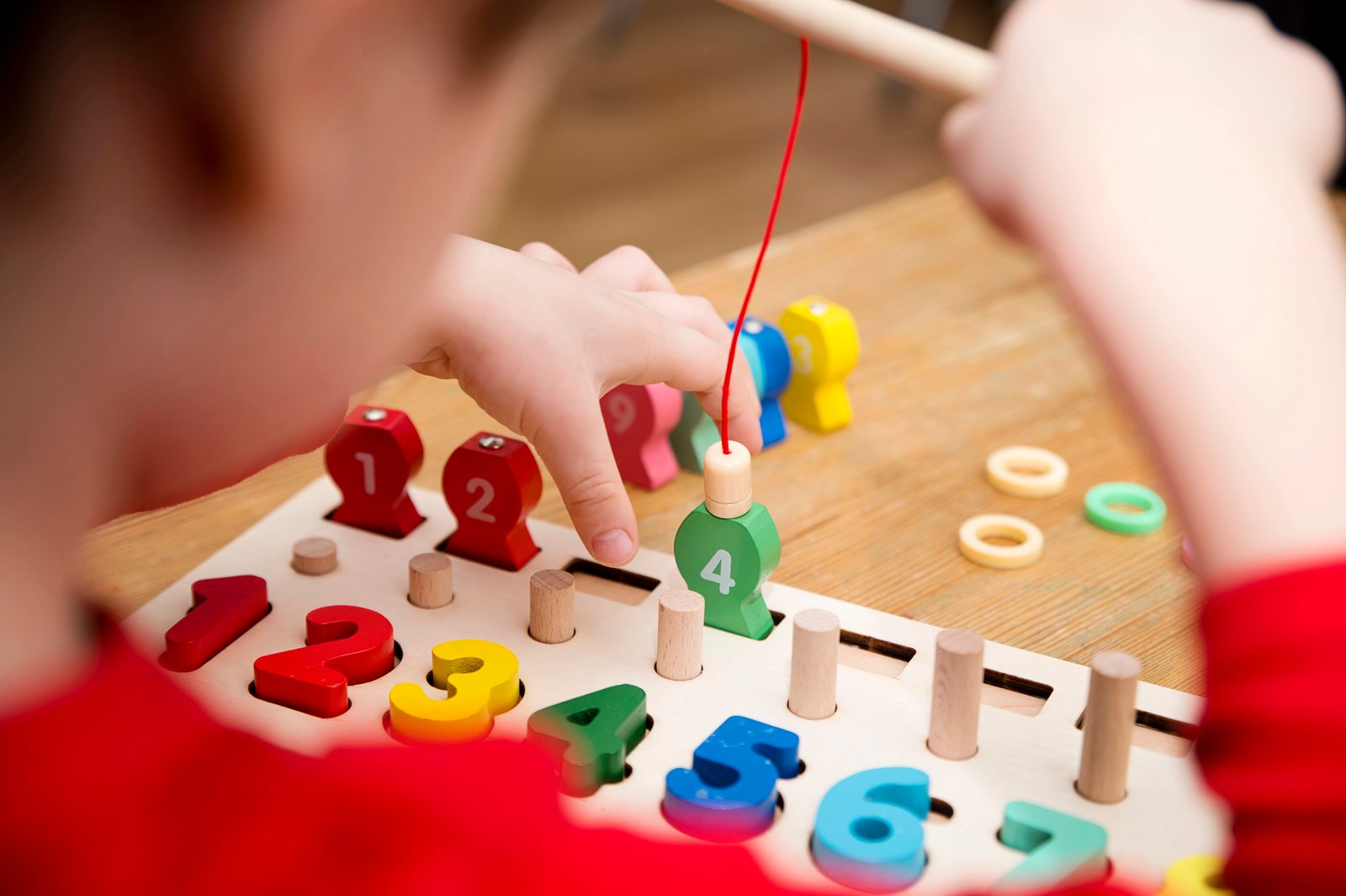 Child playing with different color wooden rings. Sequence, fine motor skills, therapy task for education and brain exercise. Counting math play game. Montessori type implement. Wooden toys.